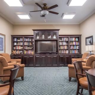 A cozy library room with bookshelves, armchairs, and a central television.