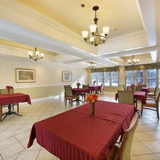 A spacious and elegantly decorated dining room with multiple tables covered in red tablecloths, featuring chandeliers and large windows.