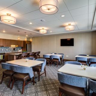 A modern conference room with multiple tables and chairs, featuring stylish lighting fixtures and a wall-mounted television.