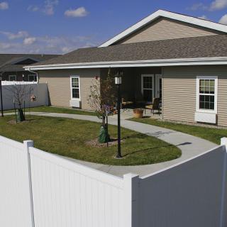 A cozy backyard with a white fence surrounding a well-maintained lawn and patio area.