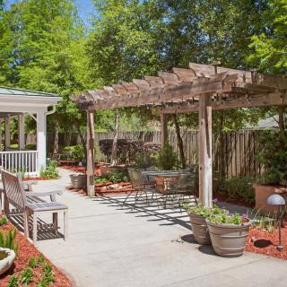 A beautiful garden features a wooden pergola and a gazebo, surrounded by lush greenery and outdoor seating.