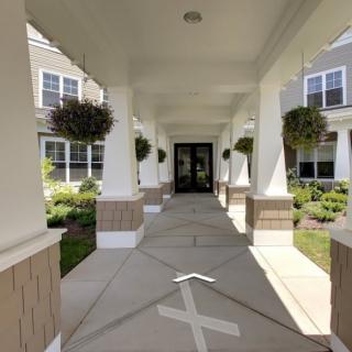 A covered walkway leads to the entrance of a building, flanked by decorative columns and landscaping.