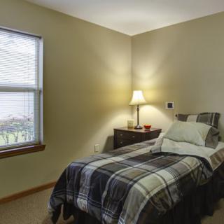 A cozy bedroom with a single bed and a warm lamp on the nightstand.