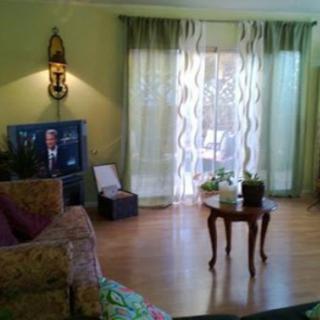 A cozy living room with a television, sofa, and a small table near the window with curtains.