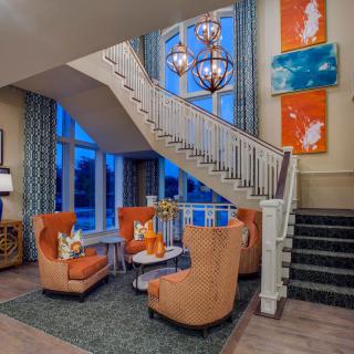 A modern lobby area featuring vibrant orange chairs, a stylish staircase, and colorful artwork on the walls.