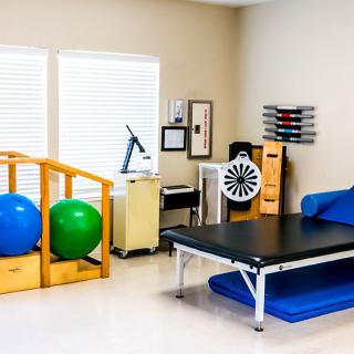 A physical therapy room equipped with exercise balls, a treatment table, and various rehabilitation tools.