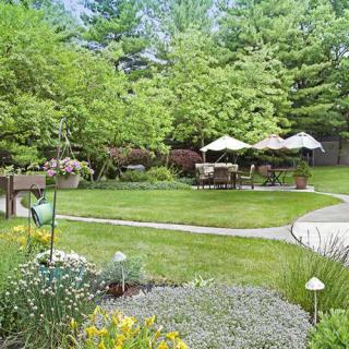 A lush garden with vibrant greenery, featuring patio furniture under umbrellas.