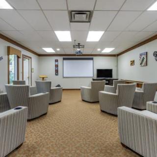 A modern conference room with a projector screen, television, and comfortable seating.