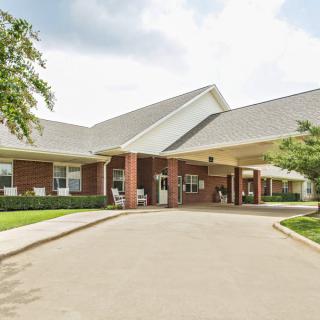 A view of a residential building entrance with a driveway and landscaped surroundings.