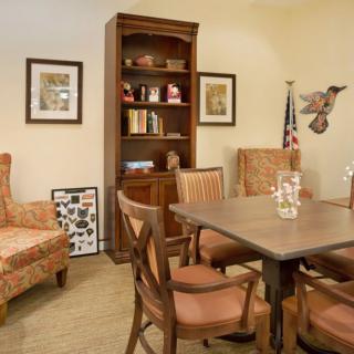 A cozy office space featuring a wooden table with chairs, a bookshelf, and decorative artwork on the walls.