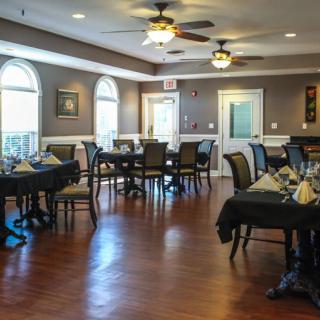 An elegant dining area with neatly arranged tables and chairs, featuring wooden floors and ceiling fans.