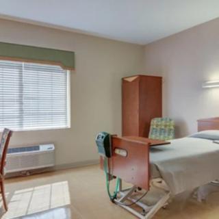 A clean and simple hospital room with a bed, chair, and window.