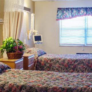 A hospital room with two patient beds, floral bedspreads, and medical equipment.