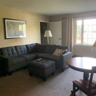 A cozy living room with a sectional sofa, coffee table, and lamp near the window.