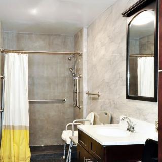 An accessible bathroom featuring a shower with grab bars, a chair, and a sink with a mirror.