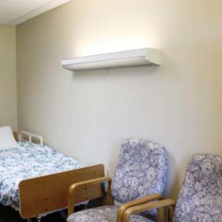 An empty hospital room with a bed and two patterned chairs.