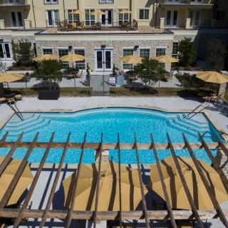 A luxury hotel with an outdoor pool, surrounded by lounge chairs and umbrellas under a wooden pergola.