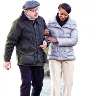 An elderly man is being assisted while walking outdoors.