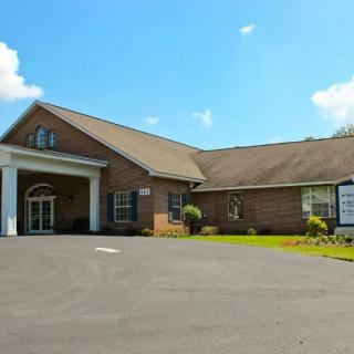 A brick building with a gabled roof and adjacent parking area under a clear blue sky.