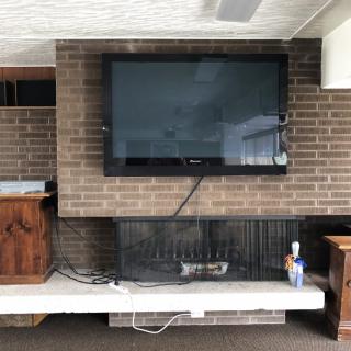 A living room with a television mounted above a brick fireplace, surrounded by various electronics and decor.