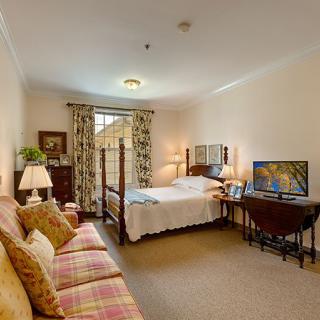 A cozy bedroom with a bed, sofa, and television, decorated warmly.