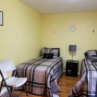 A cozy bedroom with two single beds, a folding chair, and a small bedside table against yellow walls.