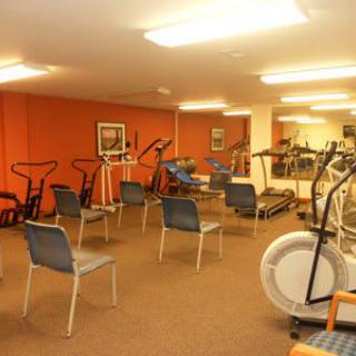 An indoor gym featuring various exercise equipment and chairs arranged in a well-lit room.