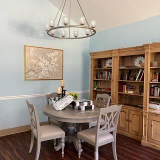 A cozy dining room with a round table, wooden bookshelf, and a chandelier.