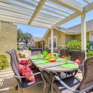 A bright outdoor patio dining area under a pergola, featuring a table set with colorful place settings and surrounded by comfortable chairs.
