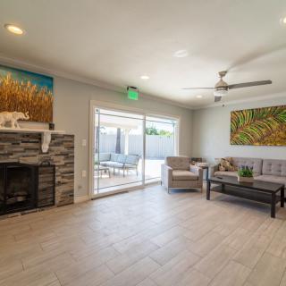 A modern living room with a fireplace, comfortable seating, artwork on the walls, and a sliding glass door leading to an outdoor area.
