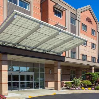 Entrance of a modern hotel building with a large glass awning and landscaped surroundings.