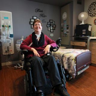 A person in a wheelchair smiling in a cozy hospital room.