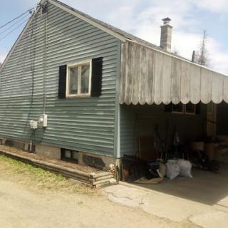 A quaint green house with a garage and an awning.