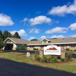 A healthcare facility with a sign in front, set against a clear blue sky with scattered clouds.