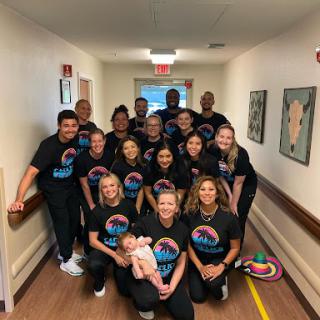 A cheerful team of healthcare professionals gathered together in a hallway, showcasing their team spirit with matching t-shirts.