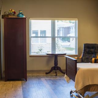 A cozy room featuring a bed, chair, wardrobe, and a window that allows natural light to fill the space.