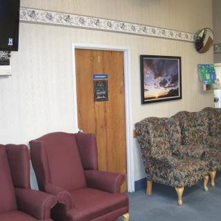 A waiting room with a mix of upholstered chairs, a wall-mounted television, and framed artwork.