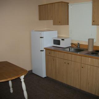 A simple kitchen setup with a refrigerator, microwave, sink, and wooden cabinets.