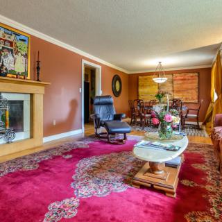 A cozy living room featuring a vibrant red carpet, comfortable seating, and a fireplace adorned with art.