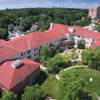 An aerial view of a large building with red rooftops, surrounded by green trees and garden areas.