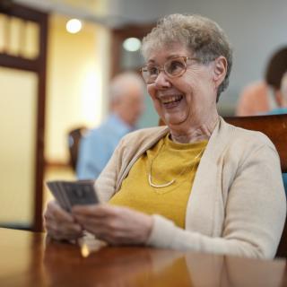 An elderly woman smiling while playing cards indoors.