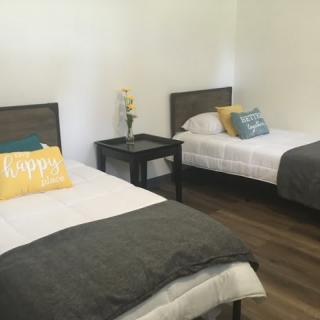 A minimalist bedroom with two beds, each adorned with pillows and a nightstand in between.