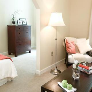 A cozy bedroom with a lamp, chair, and dresser.