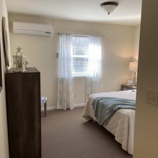 A cozy bedroom with a neatly made bed, dresser, and window with sheer curtains.