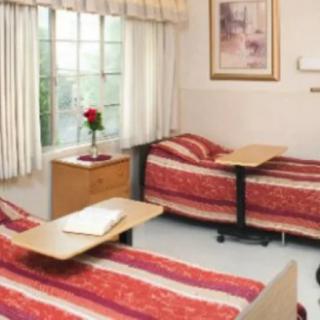 A hospital room with two beds, each equipped with a small table, and a window with curtains.