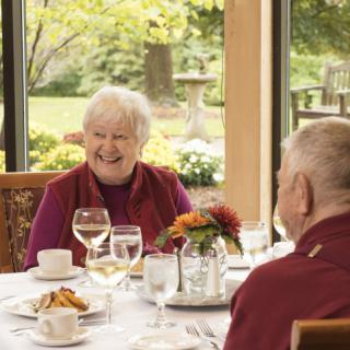 Elderly individuals enjoying a meal and conversation in a bright, indoor dining setting.