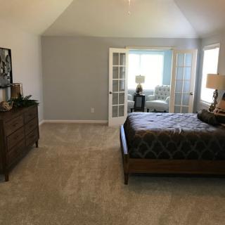 A spacious bedroom with a bed, dresser, and large windows allowing natural light.