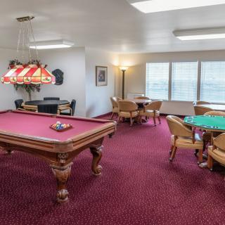 A recreational game room featuring a pool table and multiple card tables on a red-carpeted floor.