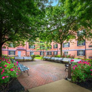 A peaceful courtyard with benches surrounded by lush greenery and a brick building.