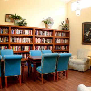 A cozy library space featuring a large bookshelf, a table with blue chairs, and a comfortable armchair.